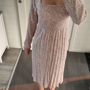 Ljusrosa blommig klänning med lång ärm - Supersöt ljusrosa klänning med små vita blommor och smockad midja. Klänningen har lång ärm, fyrkantig ringning och faller till knäna. Från only i storlek xs. Perfekt för vår och sommar!