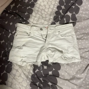 Vita jeansshorts från SOIN - Säljer ett par vita lågmidjade jeansshorts från SOIN med fransiga kanter och slitna detaljer framtill. Shortsen har fem fickor och klassisk knappgylf. Perfekta för varma dagar och en avslappnad stil. Säljer då de är för små.💕Ge förslag på ett bra pris!