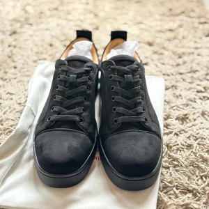 Svarta sneakers från Christian Louboutin - Snygga svarta sneakers från Christian Louboutin i mocka med klassisk röd sula och diskret logga undertill. Skorna har rund tå, svarta snören och en stilren design som sticker ut med den ikoniska röda undersidan.