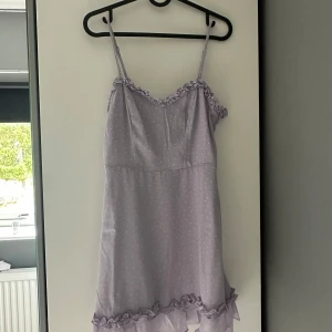 Ljuslila kortklänning från NA-KD - Supersöt ljuslila kortklänning från NA-KD x Pamela med tunna axelband, volangdetaljer vid halsringning och fåll samt små vita fjärilar som mönster. Klänningen har en feminin passform och dragkedja i sidan. Perfekt för sommarens alla tillfällen!