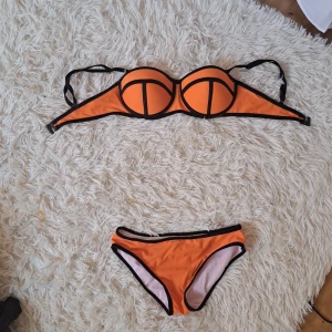 Orange bikini med svarta kanter, S - Low waist Snygg orange bikini med svarta kontrastkanter och bygel-bh med vadderade kupor.Underdelen har klassisk bikini-trosa modell. Perfekt för stranden eller poolen, riktigt poppig färg som sticker ut. Materialet är stretchigt och snabbtorkande syntet. Med avtagbara axel band❤️