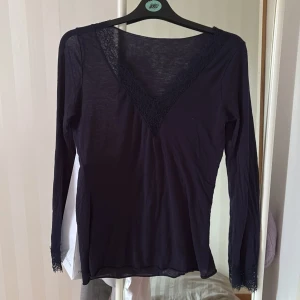 Mörkblå tröja från Intimissimi - Supersnygg mörkblå tröja från Intimissimi med v-ringning och spetsdetaljer vid halsringning och ärmslut. Tunn och mjuk i materialet, perfekt för lager-på-lager. Långärmad och sitter snyggt på kroppen. Perfekt för dig som gillar stilrena och feminina plagg.