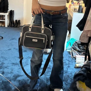 Svart axelväska från FILA med holografiska detaljer - Säljer en svart axelväska från FILA med holografiska handtag och detaljer. Väskan har både handtag och justerbar axelrem, samt flera fack med dragkedja. Perfekt för att bära med sig det viktigaste i vardagen. Ca 40x20 cm men de bilden för en bättre storleksuppfattning❤️