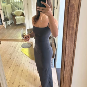 Svart långklänning från Skims - Säljer en svart långklänning från Skims i modellen Fits Everybody Long Slip Dress. Klänningen har smala axelband, figurnära passform och är tillverkad i ett mjukt, stretchigt material som sitter snyggt på kroppen. (AI genererad text)