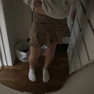 Leopardmönstrad volangkjol från Zara - Supersnygg kort kjol från Zara i leopardmönster. Kjolen har volang nertill och en figurnära passform med dragkedja i sidan. Materialet är mjukt och lätt, perfekt för att sticka ut med en trendig look.Det finns shorts under.Aldrig nånsin använt ute