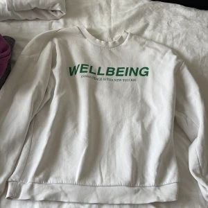 Vit sweatshirt från Gina Tricot - Vit sweatshirt från Gina Tricot med grön text 'WELLBEING' framtill. Tröjan har rund hals, ribbade muddar och är långärmad. Mjuk insida och relaxed fit, perfekt för chill dagar.