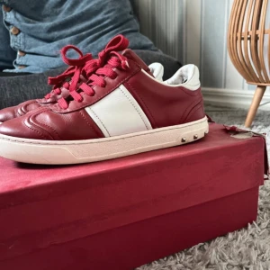 Valentino Garavani röda sneakers - Snygga röda och vita sneakers från Valentino Garavani med klassisk design och coola nitar på sulan. Skorna har snörning, rund tå och är tillverkade i skinn. Perfekta för dig som vill sticka ut med en lyxig touch och sportig vibe. Man får med allt og box snören dustbag. Skriv om det åt något du undrar över😊 pris kan sänkas 