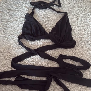 Svart bikini med långa knytband - Säljer en svart bikini med trekantsmodell och extra långa knytband som kan lindas runt midjan. Bikinin har en stilren design och passar perfekt för stranden eller poolen. Toppen har justerbara band för bästa passform.