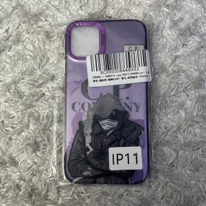 Lila mobilskal med tryck från C.P. Company - Säljer ett lila mobilskal till iPhone 11 med tryck av en person i jacka och huva på baksidan. Skalet har en glansig finish och är dekorerat med C.P. Company-loggan. Perfekt för dig som vill ha ett unikt och snyggt mobilskal.