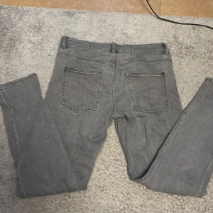Grå jeans från Kappahl, storlek 164 - Snygga grå jeans från Kappahl i storlek 164. Klassisk femficksmodell med raka ben och normal passform. Jeansen har bälteshällor och stängs med knapp och dragkedja. Perfekta till en avslappnad stil.