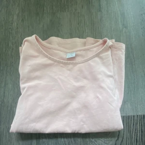 Ljusrosa volangblus från Lindex - Supersöt ljusrosa blus från Lindex med korta ärmar och volang nedtill. Tillverkad i mjuk bomull, perfekt för dig som gillar en enkel men gullig stil. Rund halsringning och avslappnad passform gör den lätt att matcha med jeans eller kjol.