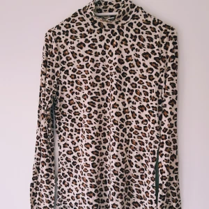 Leopardmönstrad polotröja från Vila strl M - Säljer en snygg leopardmönstrad polotröja från Vila i storlek M. Tröjan har lång ärm och är i mjukt, stretchigt material. Färgerna går i beige, brunt och svart och den har en tight passform med hög krage. Perfekt för dig som vill sticka ut lite extra.  Helt skick dock små noppror