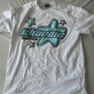 Vit Chaotic System t-shirt med stjärnor - Vit t-shirt från Chaotic System med stort tryck framtill i form av blå stjärnor och text. Klassisk passform med korta ärmar och rund halsringning. Materialet känns som bomull och trycket har en cool, grafisk vibe.