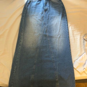Lång blå jeanskjol - Säljer en snygg lång jeanskjol från SHEIN i klassisk blå denim. Kjolen har coola sömdetaljer framtill och två bakfickor. Inga slits, helt oanvänd 