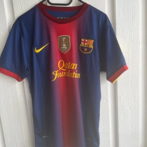 FC Barcelona Messi 10 matchtröja Nike - Säljer en klassisk FC Barcelona fotbollströja med Messi 10 på ryggen. Tröjan är blå och röd med gula detaljer, officiella klubbmärket och Qatar Foundation-tryck på bröstet. Tillverkad i lätt och ventilerande Dri-Fit-material, perfekt för fotbollsplanen eller samlingen.