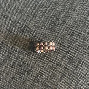 Bred ring med lila pärlor - Unik bred ring med tre rader lila pärlor som sitter tätt ihop. Pärlorna har en skimrande yta och är sammanfogade med små metallkulor. Perfekt accessoar för dig som gillar statement-smycken och vill sticka ut. Observera att bilderna inte riktigt fångar den levande och skimrande lilafärgen, men den gör sig bäst i verkligheten. Hör av dig om du vill ha fler bilder eller undrar något! 