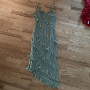 Ljusgrön volangklänning med smala band - Supersöt ljusgrön klänning med smala axelband och volanger som går diagonalt över hela klänningen. Asymmetrisk nederkant ger en extra cool touch. Perfekt för dig som vill sticka ut med en romantisk vibe.