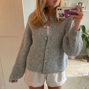 Grå stickad kofta med knappar - Supermysig grå stickad kofta med stora knappar framtill och långärmad modell. Koftan har en loose fit och är perfekt att slänga på sig över en t-shirt. Tjockt garn och ribbad struktur ger en chill och trendig vibe.