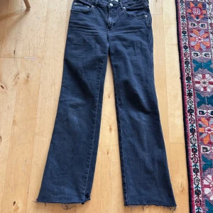 Svarta bootcut jeans  90's Boot - Svarta jeans från modellen 90's Boot med bootcut-ben och råa, fransiga benslut. Klassisk femficksdesign och knappgylf. Jeansen har en mörk tvätt och är tillverkade i mjukt denimtyg som ger en skön vintagekänsla.