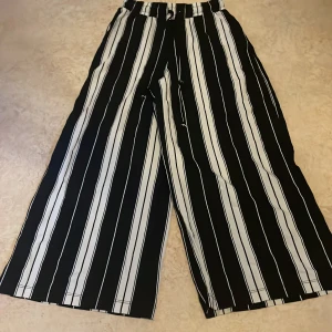 Svartvita randiga wide byxor XS - Säljer ett par svartvita byxor från Gina Tricot i storlek XS. Byxorna har breda ben, vertikala ränder och resår i midjan med snörning. De är tillverkade i ett mjukt och lätt material som känns skönt mot huden. Perfekta för en chill och trendig look.