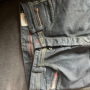 Mörkblå Diesel jeans straight fit - Säljer ett par mörkblå jeans från Diesel med raka ben och snygga kontrastsömmar i gult. Klassisk femficksmodell med dragkedjedetalj på myntfickan. Jeansen är i bomull och har en clean, tidlös look.