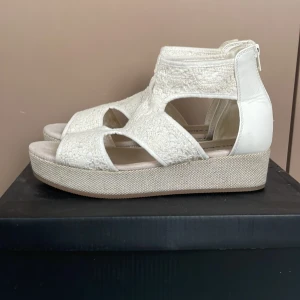 Vita spets sandaler  - Snygga vita sandaler från Din Sko i storlek 38 med broderad textil och detaljer i syntet. Skorna har öppen tå, platåsula och dragkedja bak. Har använt två gånger. Priset kan diskuteras 💞