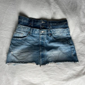 Blå jeanskjol med dubbel midja från Zara - Cool blå jeanskjol från Zara med unik dubbel midja och råa kanter nertill. Kjolen har klassiska fickor fram och bak, bälteshällor och slitna detaljer. .