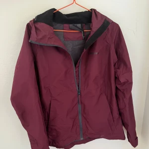 Vinröd vindjacka från Everest - Snygg vinröd vindjacka från Everest med huva och hel dragkedja framtill. Jackan är tillverkad i lätt polyester och har meshfoder på insidan för extra komfort. Perfekt för blåsiga dagar och enkel att packa ner i väskan. Stilsäker och funktionell för uteliv.