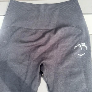 Svarta leggings från Peach Tights  - Svarta leggings från Peach Tights med hög midja och scrunch-detalj bak. Tillverkade i stretchigt material av 87% nylon och 13% spandex. Diskret logga framtill och 'peach' tryckt bak i midjan. Perfekta för träning eller chill.