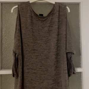 Grå loose tröja med knytärmar - En grå, loose-fit tröja med knyt på ärmarna. Tröjan har en avslappnad passform och är tillverkad i ett mjukt material. Perfekt för dig som gillar en chill och enkel stil.