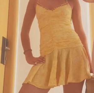 Gul kort sommarklänning med spaghettiband - Superfin gul kort klänning med smala spaghettiband och lätt rynkad överdel. Kjolen är utsvängd och materialet ser lätt och luftigt ut, perfekt för varma dagar. Söt detalj vid urringningen och figurnära passform.