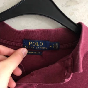 Vinröd pikétröja Polo Ralph Lauren - Snygg vinröd pikétröja från Polo Ralph Lauren i bomull. Klassisk krage, korta ärmar och broderad logga på bröstet. Modellen är slim fit och passar perfekt till en avslappnad men stilren look.