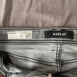 Replay jeans grå - Säljer ett par Replay Rocco jeans i ljusgrå tvätt med klassisk femficksdesign. Jeansen har comfort fit, raka ben och dragkedja i gylfen. Snygga kontrastsömmar och diskret Replay-logga på insidan. Perfekta för dig som gillar stilrena och bekväma jeans.