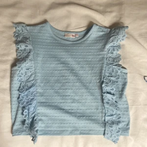 Ljusblå topp med spetsvolang - Supersöt ljusblå topp, från barnavdelningen men kan jämföras med xxs/xs i damstorlek. Knappt använd. 