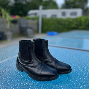 Svarta chelsea boots i skinn - Stilrena svarta chelsea boots i äkta skinn med klassisk rund tå och låg klack. Snygga detaljer med resår på sidorna och dragkedja för enkel påtagning. Perfekta för dig som gillar en tidlös look med edge.