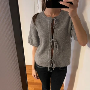 Grå stickad kofta med snörning - Superfin grå stickad kofta med korta ärmar och tre snörningar framtill som passar till allt. Den har används ett fåtal gånger💕