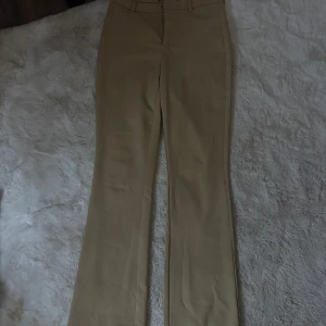 Beiga bootcut kostymbyxor Vero Moda - Snygga beiga kostymbyxor från Vero Moda med bootcut-snitt. Byxorna har hällor för bälte och klassisk midja. Perfekta för en clean och stilren look, matcha med sneakers eller klackar för att höja outfiten.