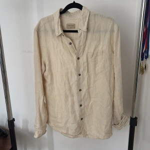 Beige linneskjorta Studio Total M - Snygg beige skjorta från Studio Total i luftig linnemix. Klassisk krage, bröstficka och knappar framtill. Perfekt för dig som gillar en avslappnad och stilren look. Långärmad modell med normal passform.