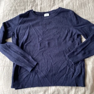Mörkblå stickad tröja från Vila - En enkel och stilren mörkblå stickad tröja från Vila. Tröjan har rund halsringning, långa ärmar och ribbade muddar vid ärmslut och nederkant. Lite nopprig 