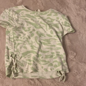 Grönvit ribbad topp med snörning H&M - Superfin ribbad topp från H&M i vitt och ljusgrönt med coolt zebramönster. Kortärmad modell med snörningsdetaljer i sidorna som ger en extra snygg touch. Perfekt för dig som gillar trendiga och unika plagg. Liten fläck i back, har inte provat att tvätta.