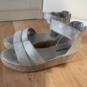Silvriga sandaler med platåsula - Snygga sandaler i metallic-silver med breda remmar och platåsula i flätad jute. Perfekta för att lyfta sommarlooken med lite extra höjd och glans. I princip oanvända. 