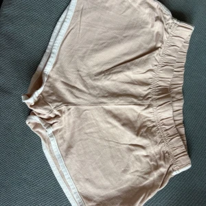 Rosa shorts - Snygga rosa/aprikos färgade shorts med vit kant och elastisk midja. De har en sportig vibe och är perfekta för varma dagar. Mjukt material som känns skönt mot huden och en loose passform som ger en avslappnad look.