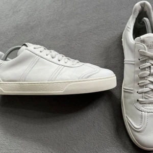 Vita Valentino Garavani sneakers - Stilrena vita sneakers från Valentino Garavani i mjukt skinn. Klassisk låg modell med rund tå, vita snören och diskreta sömdetaljer. Perfekta för dig som gillar minimalistisk och lyxig stil.