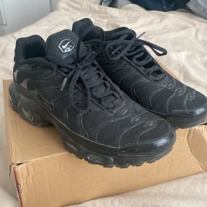  Nike Air Max Plus TN sneakers - Svarta Nike Air Max Plus TN sneakers med ikonisk Tn-detalj på hälen och vågiga mönster på ovandelen. Skorna har snörning, mesh och syntetmaterial samt en chunky sula med synliga Air Max-enheter för extra komfort och streetkänsla.
