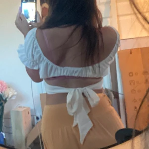 Vit croppad blus med knyt i ryggen - Supersöt vit croppad blus med puffiga korta ärmar och bred knytning i ryggen. Toppen har en omlottkänsla framtill och är perfekt för varma dagar. 