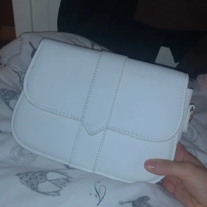 Vit axelväska i skinnimitation - fin vit axelväska, axelband följer med! Väskan kommer knte till anvöndning då jag var många andra vita väskor. Väskan levererades till mig med små defekter därav priset. 