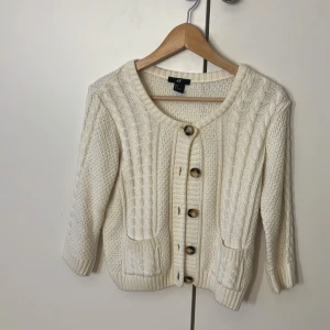 Vit stickad kofta från H&M, S - Superfin vit stickad kofta från H&M i storlek S. Koftan har snygga kabelstickade detaljer framtill, ribbade muddar och stora knappar. Den har två små fickor fram. Perfekt att slänga över en topp för en chill look.