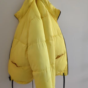 Gul pufferjacka med dragkedja - Snygg gul pufferjacka med dragkedja och två fickor framtill. Jackan är vadderad och har en oversized look, perfekt för kalla dagar. Färgen är riktigt poppig och ger en cool vibe till din outfit. Passar dig som vill sticka ut och hålla dig varm.