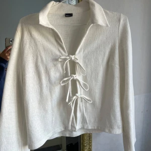 Vit blus med knytning - Säljer en stilren vit blus med unik knytning framtill. Blusen har långa ärmar och en klassisk krage, perfekt för en chic look. Passar bra till både jeans och kjol.