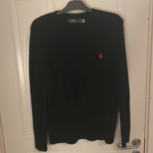 Svart stickad tröja från Polo Ralph Lauren - Säljer en stilren svart tröja från Polo Ralph Lauren med det klassiska röda logotypen på bröstet. Tröjan har långa ärmar och är perfekt för en elegant och avslappnad look. 10/10 skick. Kom privat för frågor!!!